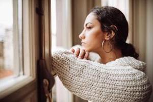 young pensive woman leaning on window and gazing out